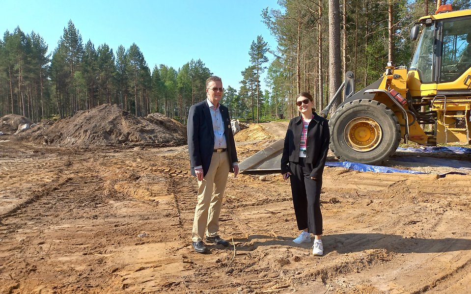 Conny Axelsson och Neira Dedic vid det nya bostadsområdet i södra Hovmantorp. I bakgrunden syns en gul grävmaskin, tallar och jordmassor. Foto.